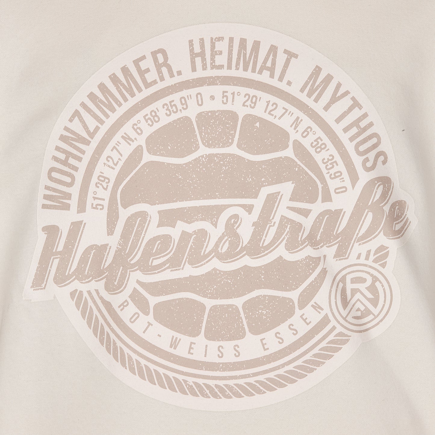 Nahaufnahme großer Druck auf Vorderseite, Brusthöhe, rund; Fußball in hellbraun, darum angeordnet die Koordinaten des Stadions, darum eine Kordel und außen die Sprüche "Wohnzimmer. Heimat. Mythos" (oben) und das Logo unten rechts.