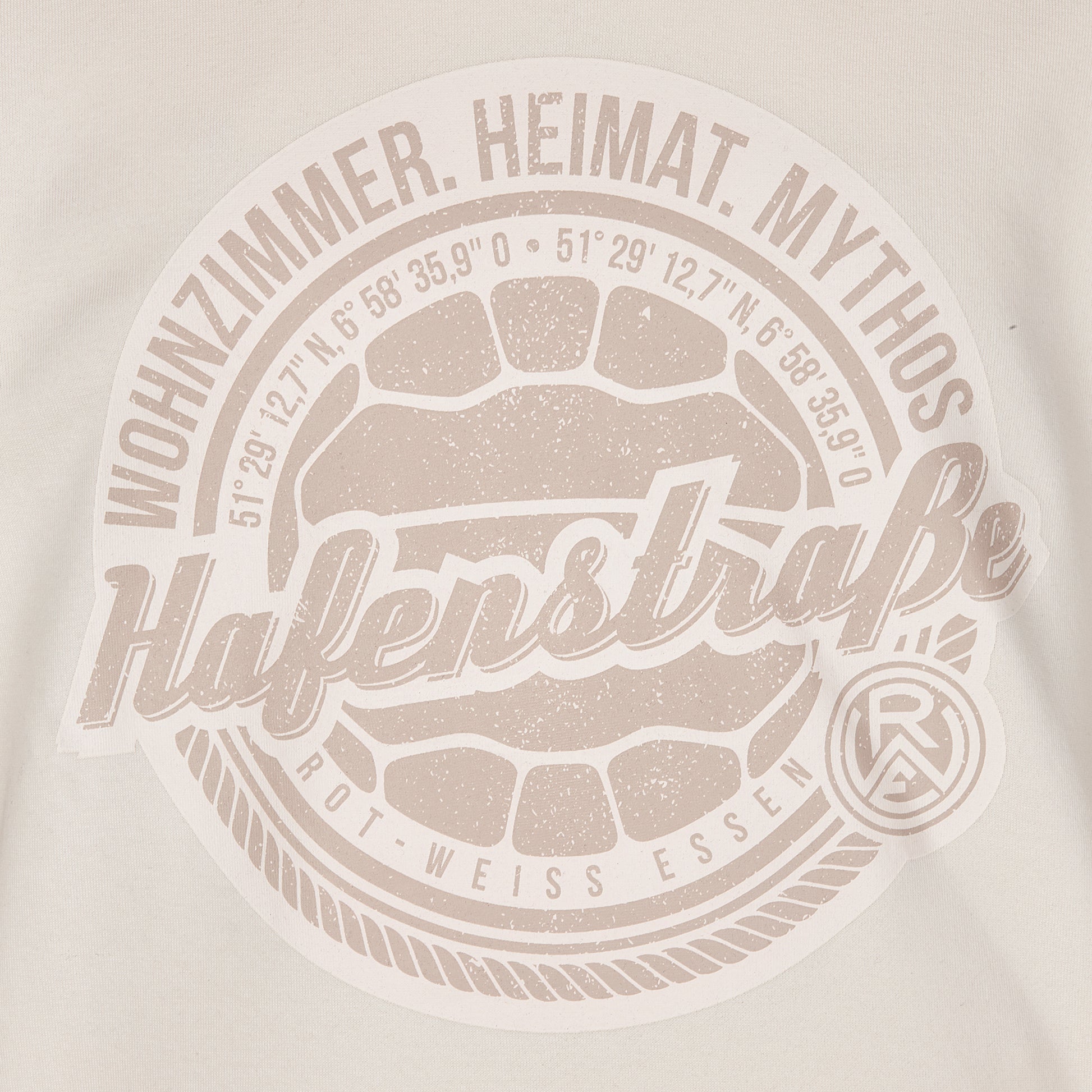 Nahaufnahme großer Druck auf Vorderseite, Brusthöhe, rund; Fußball in hellbraun, darum angeordnet die Koordinaten des Stadions, darum eine Kordel und außen die Sprüche "Wohnzimmer. Heimat. Mythos" (oben) und das Logo unten rechts.