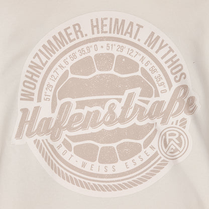 Nahaufnahme großer Druck auf Vorderseite, Brusthöhe, rund; Fußball in hellbraun, darum angeordnet die Koordinaten des Stadions, darum eine Kordel und außen die Sprüche "Wohnzimmer. Heimat. Mythos" (oben) und das Logo unten rechts.