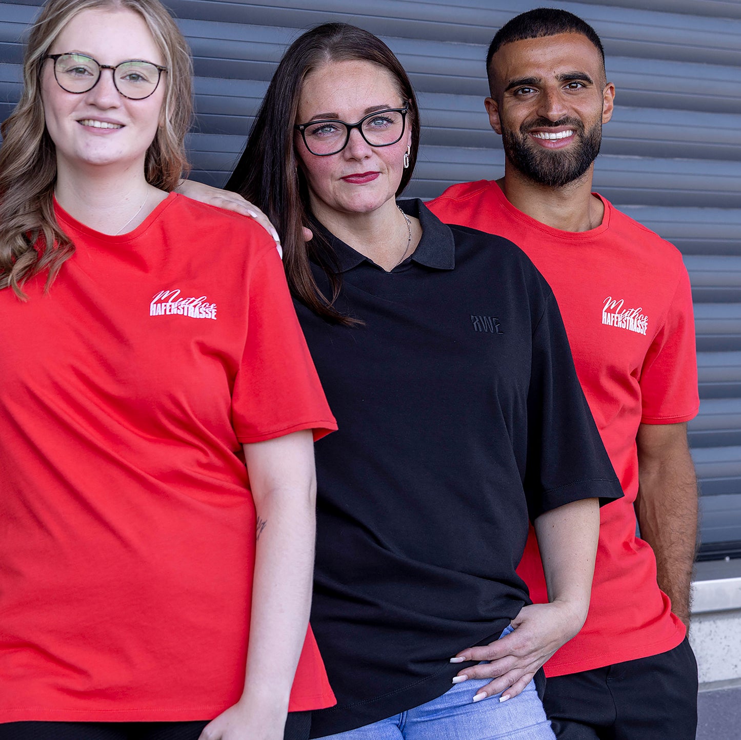 Jasmin trägt schwarzes oversize Polo mit V-Ausschnitt und "RWE" Stickerei in schwarz auf linker Brust, keine Knopfleiste