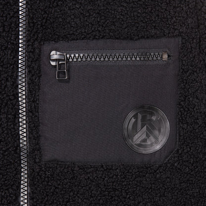 Nahaufnahme Brusttasche aus glattem Kontraststoff, mit Reißverschluss und Silikon Logo-Patch Ton-in-Ton zum Teddystoff